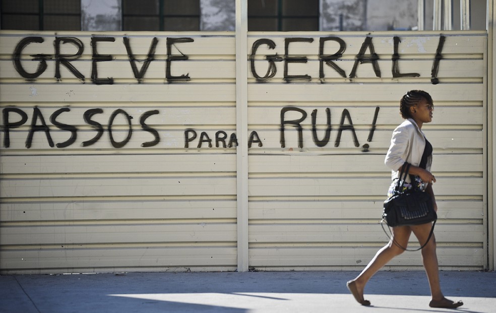 Mulher passa por mensagem em grande de rua de Lisboa convocando greve, Portugal. — Foto: PATRICIA DE MELO MOREIRA/AFP