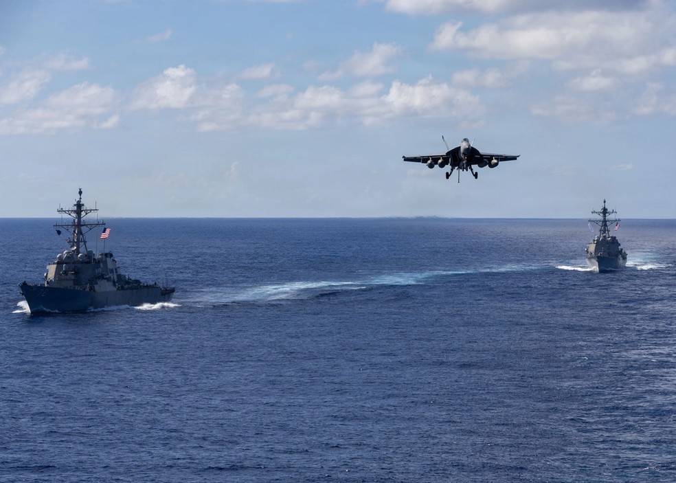 Jato F-18 se aproxima do porta-aviões USS Gerald Ford no Oceano Atlântico, com destróieres USS Mahan (à esquerda) e USS Bainbridge ao fundo em 13 de novembro de 2025. — Foto: Triniti Lersch/Marinha dos Estados Unidos