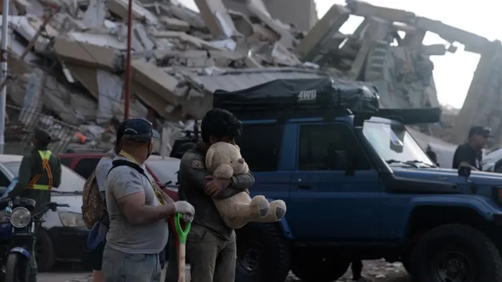 Familiares dos migrantes que foram deportados no voo 164, que chegou à Venezuela no dia dos dois terremotos (24/6), no lado de fora dos edifícios que desabaram em La Guaira — Foto: Nicole Kolster/BBC