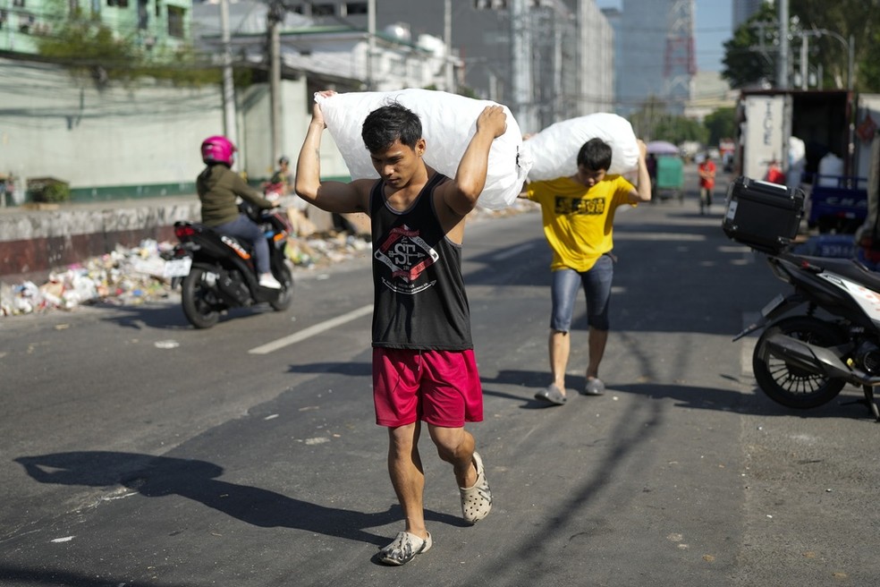 Homens entregam sacos de cubos de gelo enquanto a demanda permanece alta devido às altas temperaturas em Quezon City, Filipinas, em 24 de abril de 2024. — Foto: Imagem: Aaron Favila/Associated Press