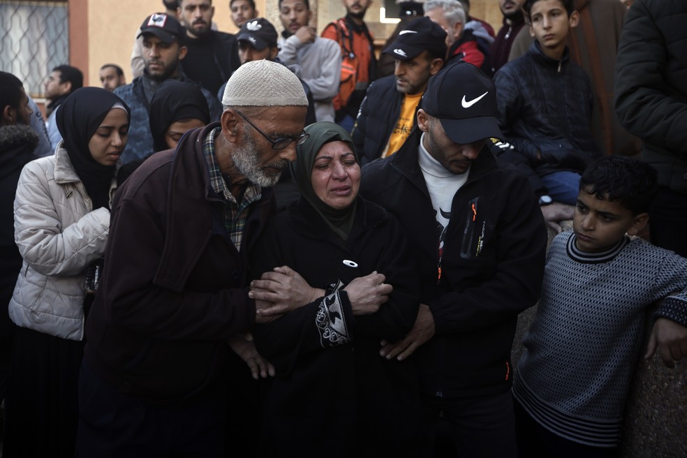 Homens palestinos auxiliam mulher que chora após bombardeio em 24 de dezembro de 2023 — Foto: Mohammed Dahman/Associated Press