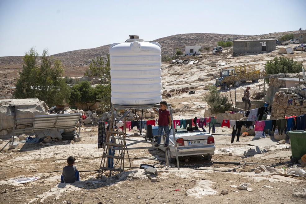 Nesta imagem de arquivo de 2021, crianças da vila de al-Mufagara, perto de Hebron, brincam em uma caixa d'água que substituiu a anterior, danificada em ataque de colonos israelenses na Cisjordânia. — Foto: Nasser Nasser/AP