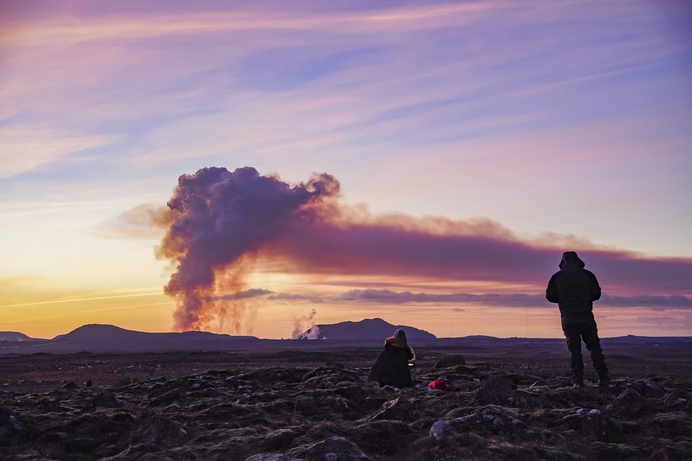 Casal observa uma coluna de fumaça sendo expelida pelo vulcão que entrou em erupção perto de Grindavík, no sudeste da Islândia, neste domingo, 14 de janeiro de 2024. — Foto: AP Photo/ Marco Di Marco