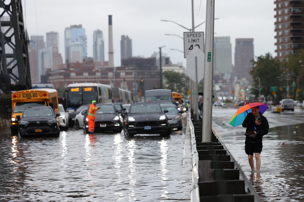 Homem caminha em rua de Nova York e carros tentam atravessa alagamento durante tempestade fora de época na cidade, em 29 de setembro de 2023. — Foto: Andrew Kelly/Reuters