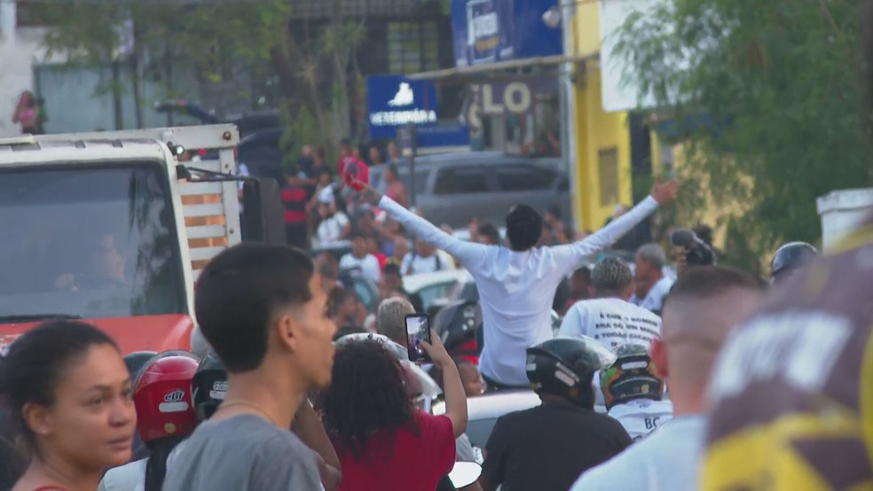 Sentado sobre um carro em movimento, Oruam acena para o público em Bangu — Foto: Reprodução/TV Globo