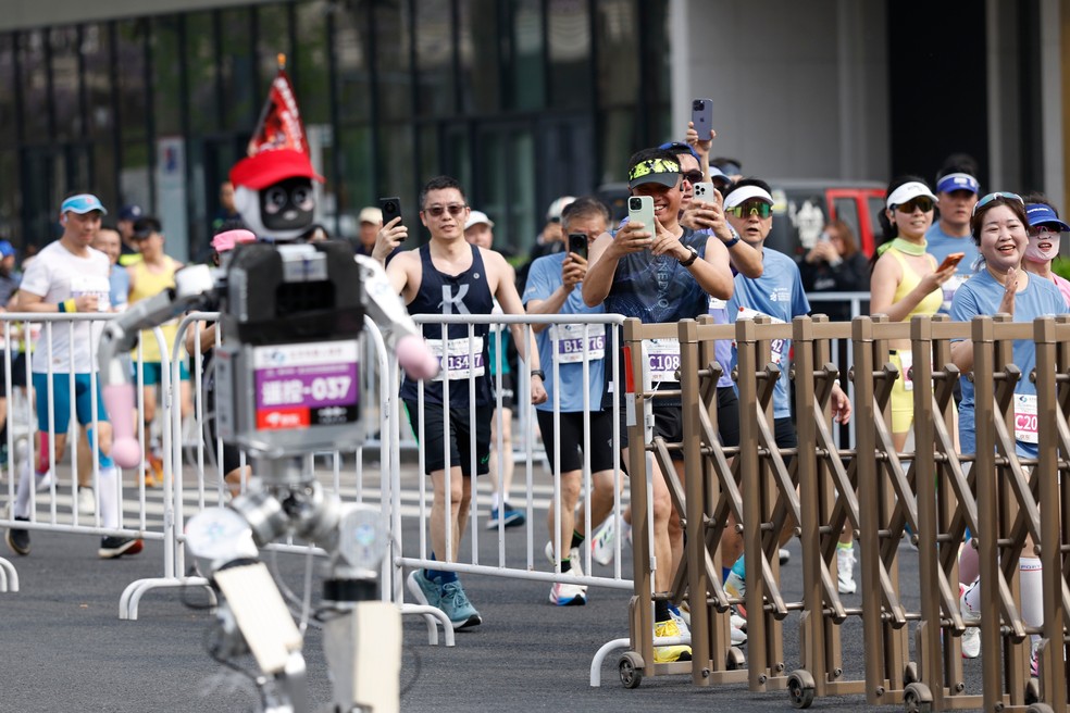 Corredores tiram fotos de robô humanoide que participou de meia-maratona em Pequim neste domingo (19) — Foto: Haruna Furuhashi/AP