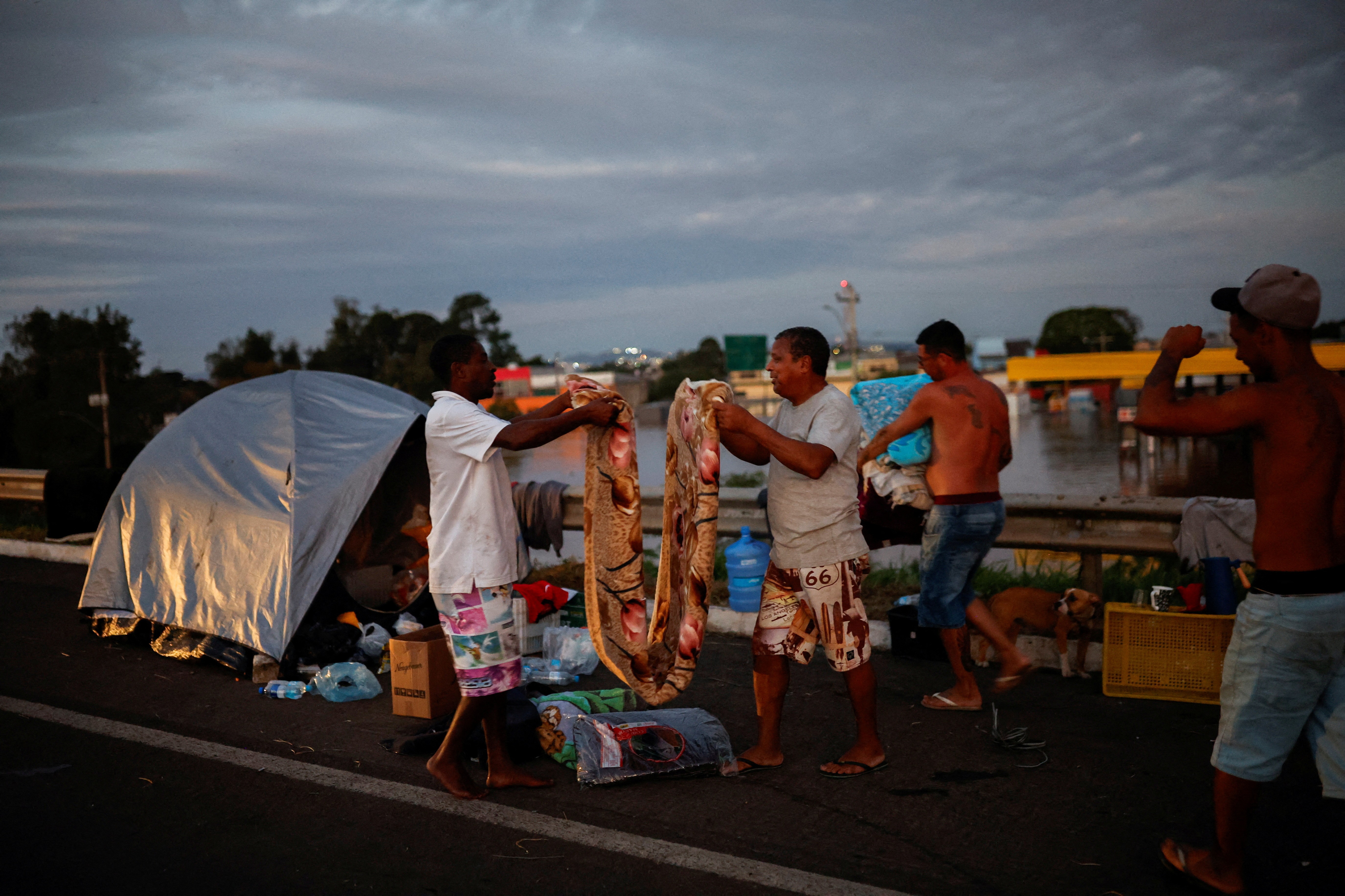 Homens dobram um cobertor enquanto acampam na estrada perto de uma rua inundada em Eldorado do Sul, no Rio Grande do Sul, Brasil, 6 de maio de 2024. — Foto: Reuters/Amanda Perobelli