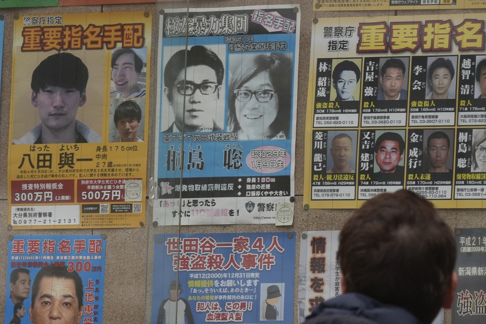 Poster de procurado com o rosto de Satoshi Kirishima (poster azul no centro) colado na parte de fora de delegacia em Tóquio. Kirishima era um dos fugitivos mais procurados do Japão desde a década de 1970. — Foto: Eugene Hoshiko/AP