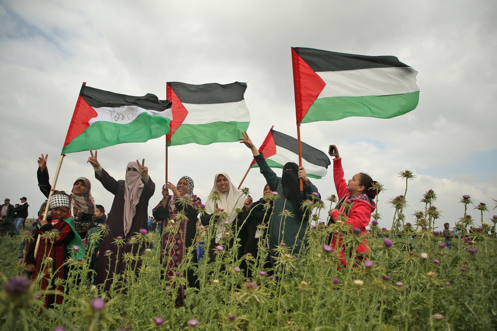 Mulheres palestinas acenam com bandeiras palestinas e mostram o gesto de vitória durante um protesto perto da fronteira com Israel, na Faixa de Gaza, em 30 de março de 2018. — Foto: Mohammed Abed/AFP