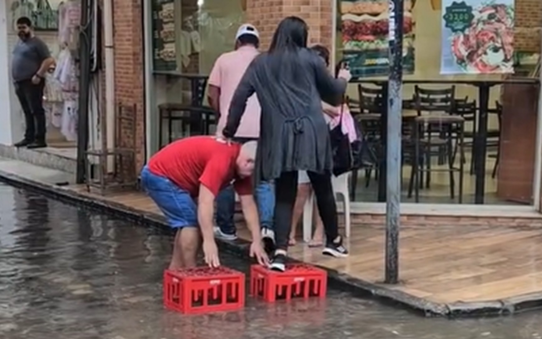 Homem improvisa ponte e ajuda pessoas a atravessar rua alagada no Centro do Recife; VÍDEO