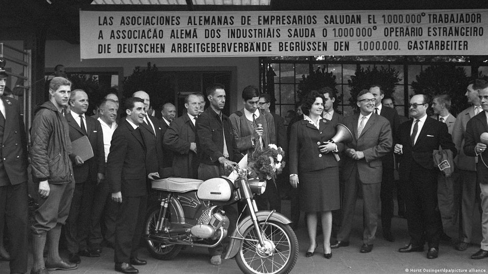 Em 1964, português Armando Rodrigues (centro) foi acolhido como o milionésimo trabalhador estrangeiro na então Alemanha Ocidental e ganhou uma moto de presente — Foto: Horst Ossinger/dpa/picture alliance