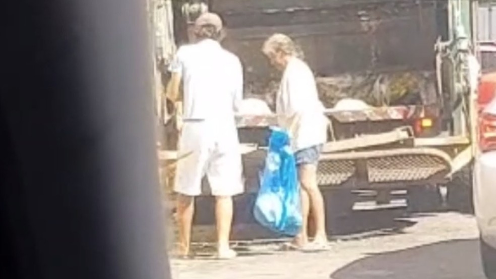 Casal aparece com saco e retira alimentos jogados de supermercado para caminhão do lixo.  — Foto: Reprodução
