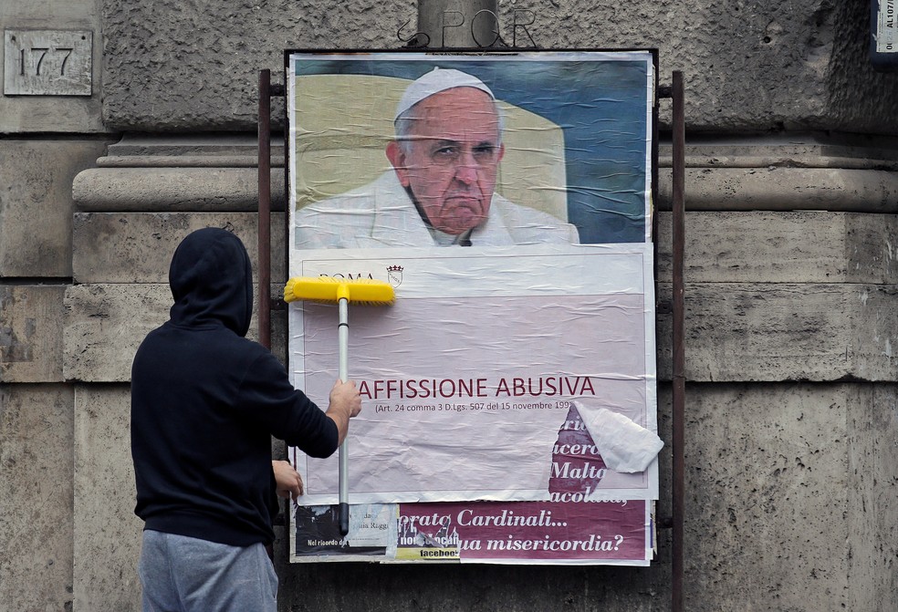 Funcionário cobre cartaz que acusa o papa Francisco de atacar católicos conservadores — Foto: REUTERS/Max Rossi