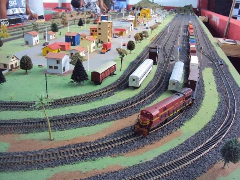 Imagem de alguns trens de brinquedo em miniatura transportando mercadorias  nos trilhos do trem próximo à vila do velho oeste