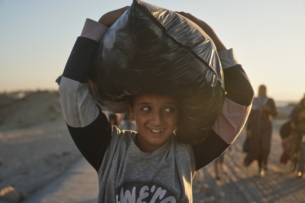 Menina palestina carrega uma sacola na cabeça enquanto caminha em direção à Faixa de Gaza, em 10 de outubro de 2025 — Foto: AP Photo/Abdel Kareem Han