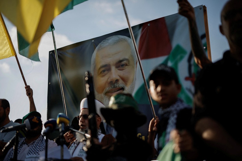 Manifestantes seguram bandeiras e armas ao lado de uma imagem do líder do Hamas, Ismail Haniyeh, durante um protesto para condenar seu assassinato no Irã, em Sidon, Líbano, nesta quarta-feira (31). — Foto: Alkis Konstantinidis/Reuters