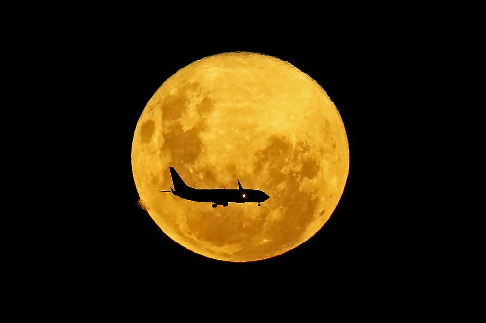 9 de março - Um avião passa em frente à lua cheia vista de Curitiba. A superlua é visível quando a lua cheia coincide com sua posição mais próxima da Terra, o que a faz parecer mais brilhante e maior que outras luas cheias — Foto: Heuler Andrey/AFP