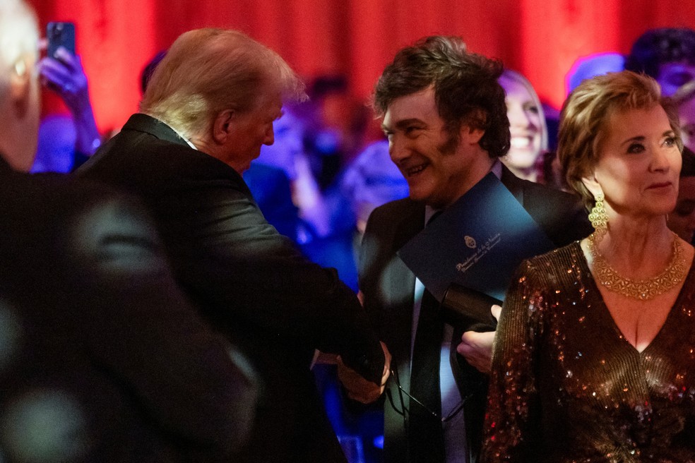 Donald Trump e Javier Milei se cumprimentam durante evento de gala na propriedade do presidente eleito dos EUA, em Mar-a-Lago, na Flórida — Foto: Carlos Barria/Reuters