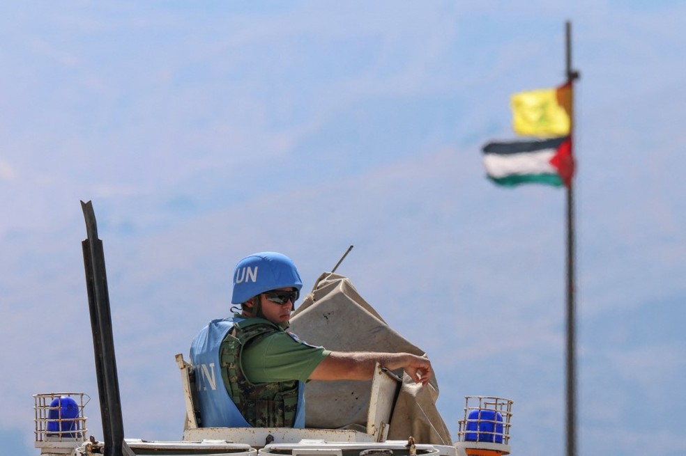 A bandeira palestina e a bandeira do Hezbollah balançam ao vento em um mastro enquanto as forças de manutenção da paz da Força Interina das Nações Unidas no Líbano (UNIFIL) patrulham a área fronteiriça entre o Líbano e Israel na colina Hamames, na área de Khiyam, no sul do Líbano, em 13 de outubro , 2023. — Foto: Joseph EID / AFP