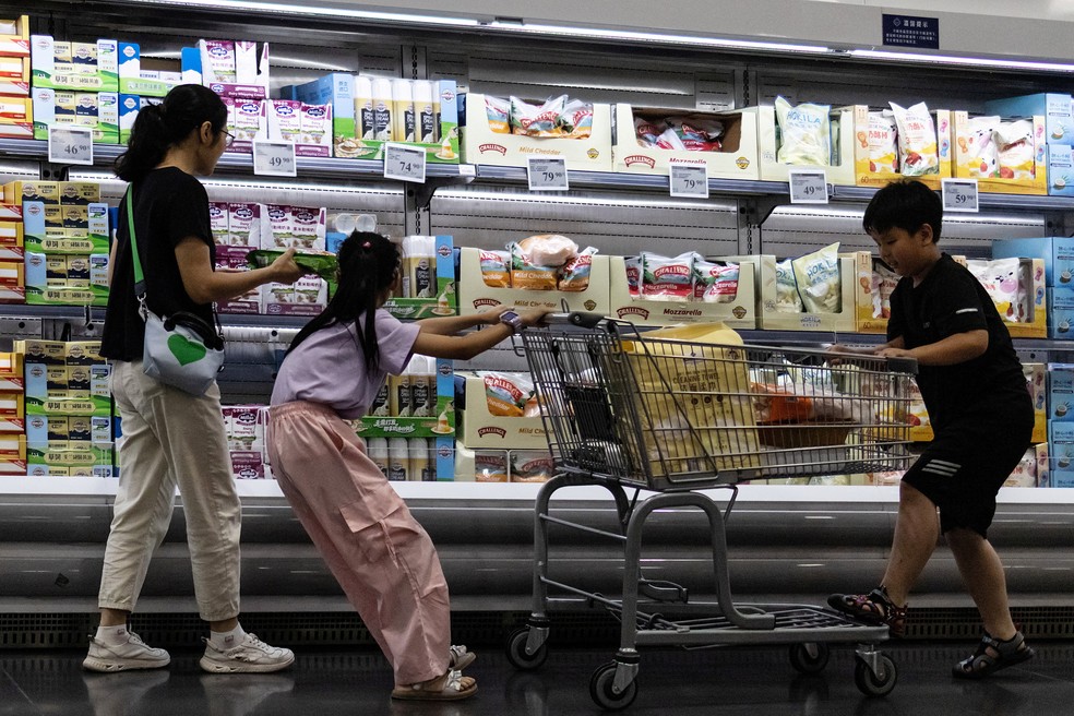 Uma mulher e duas crianças fazem compras diante de uma prateleira refrigerada de queijos em um supermercado em Pequim, na China, em 10 de julho de 2026. — Foto: Reuters