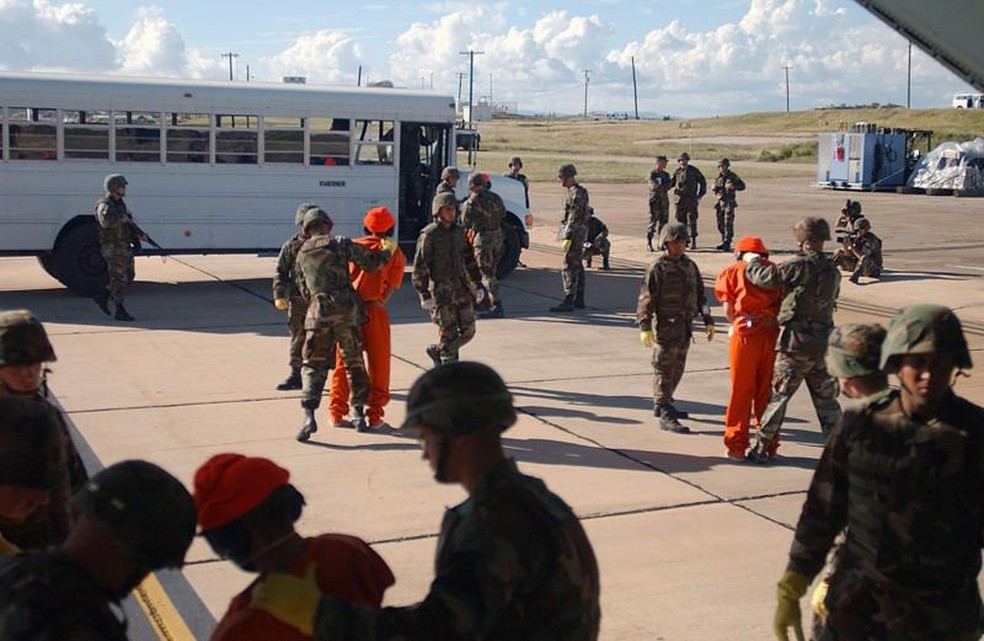 Fuzileiros navais dos EUA transportam vários prisioneiros do avião que os trouxe do Afeganistão para um ônibus que os levaria para a prisão da base de Guantánamo. — Foto: JEREMY T. LOCK/USAF via BBC