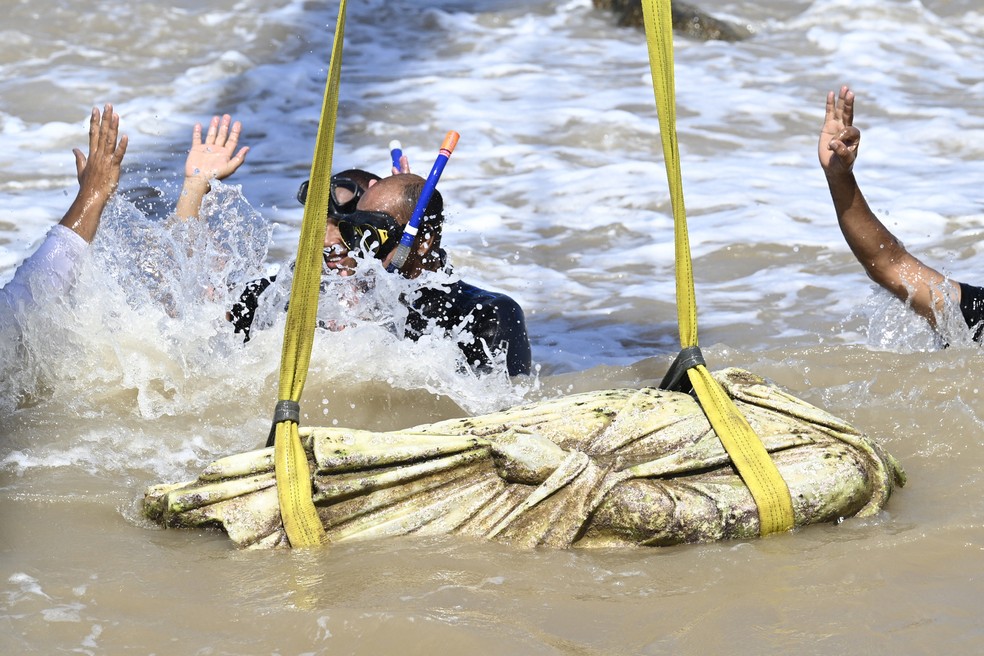 Mergulhadores comemoram enquanto um guindaste puxa um artefato das águas da baía de Abu Qir, em Alexandria, no dia 21 de agosto de 2025, como parte de um evento organizado pelo Ministério do Turismo e das Antiguidades para recuperar antiguidades submersas. — Foto: Khaled DESOUKI / AFP