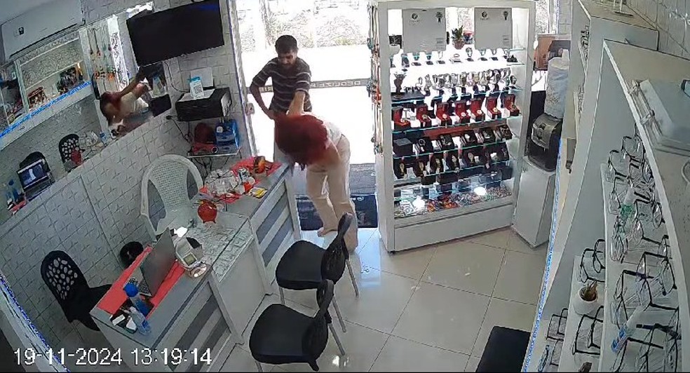 Assaltante aponta arma para cabeça de vendedora quando ela se aproxima da porta — Foto: Reprodução/WhatsApp