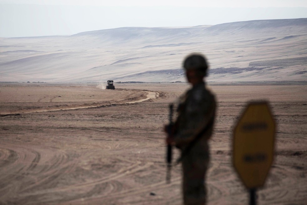 Um soldado faz guarda enquanto máquinas pesadas operam perto do posto fronteiriço de Chacalluta, na fronteira entre Chile e Peru, em 16 de março de 2026. — Foto: Foto por PATRICIO BANDA / AFP
