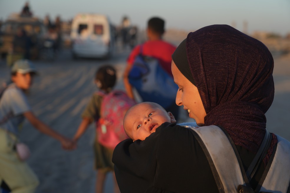 Uma mulher palestina carrega seu bebê enquanto caminha ao longo da estrada costeira para a Faixa de Gaza, em 10 de outubro de 2025 — Foto: AP Photo/Abdel Kareem Hana