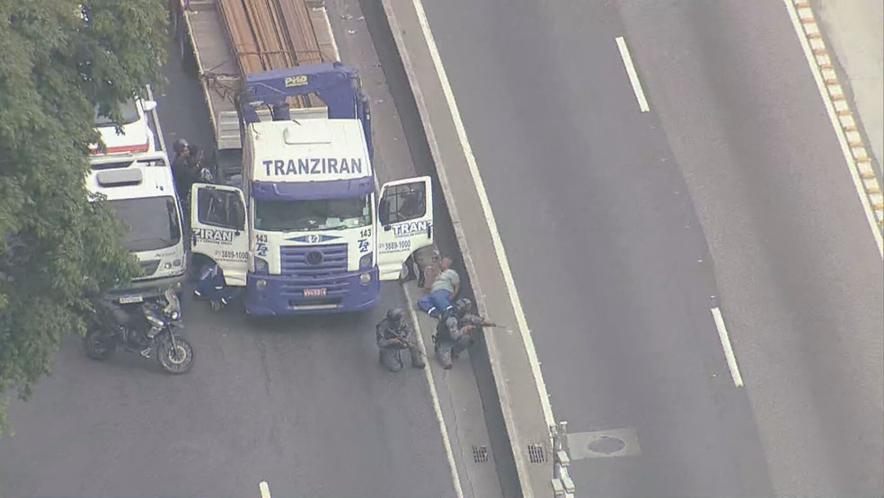 Motorista de caminhão se abaixa ao lado de mureta da Avenida Brasil — Foto: Reprodução/ TV Globo