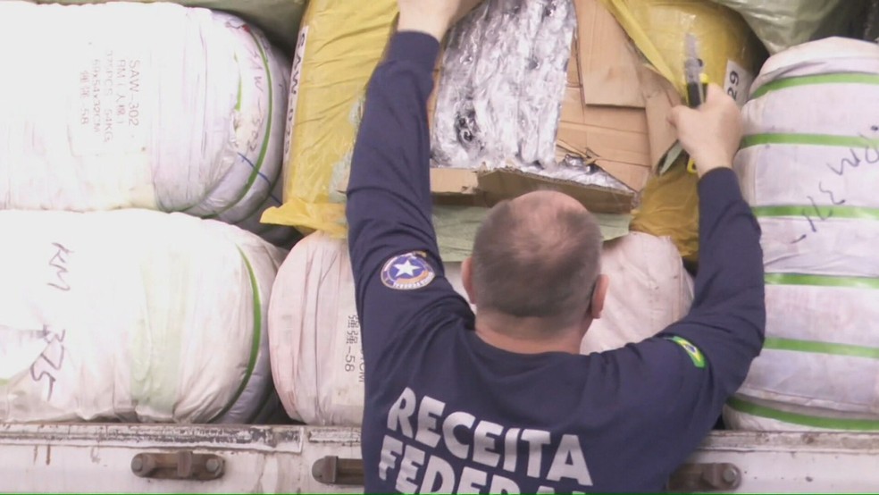 Funcionário da Receita Federal abre uma caixa com mercadorias apreendidas em Foz do Iguaçu (PR) — Foto: Reprodução/Jornal Hoje