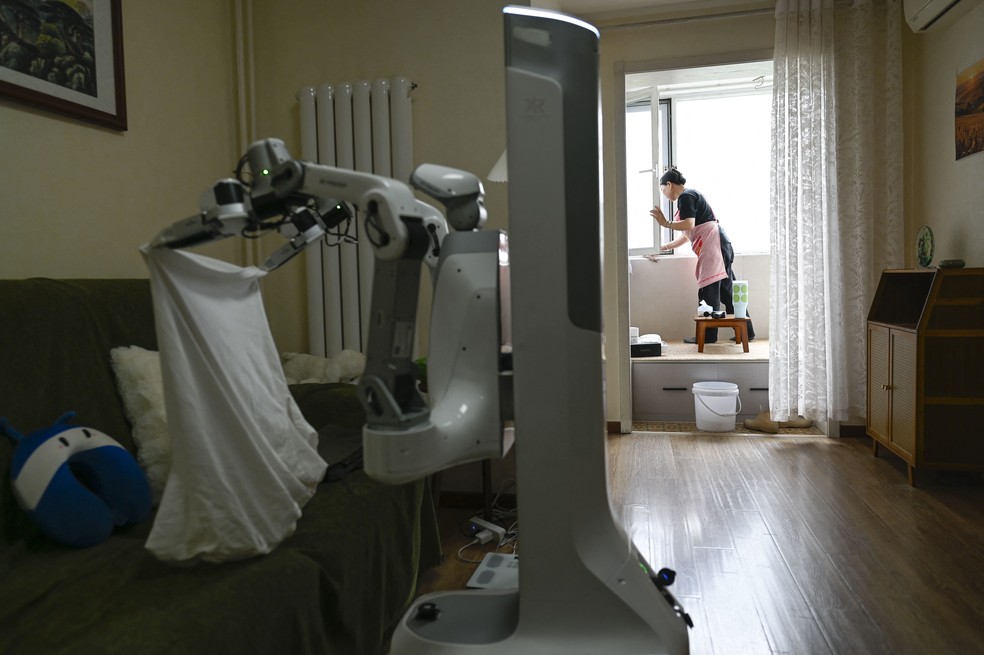 Foto tirada em 21 de maio de 2026, mostra uma empregada doméstica trabalhando ao lado de um robô da X Square na casa de um cliente em Pequim — Foto: WANG ZHAO/AFP