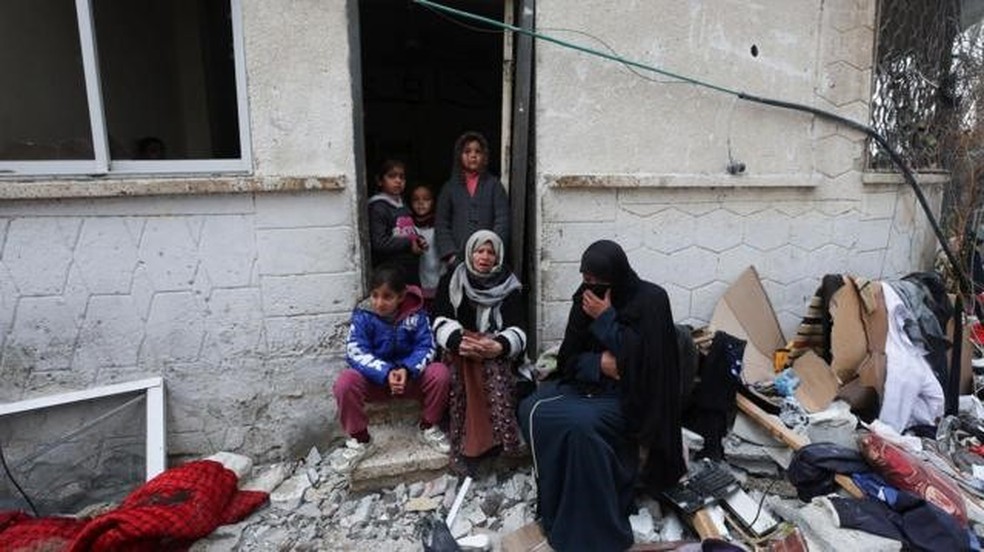 Família rodeada por destroços em Rafah após bombardeio israelense em foto desta sexta-feira (9/2) — Foto: REUTERS/IBRAHEEM ABU MUSTAFA via BBC