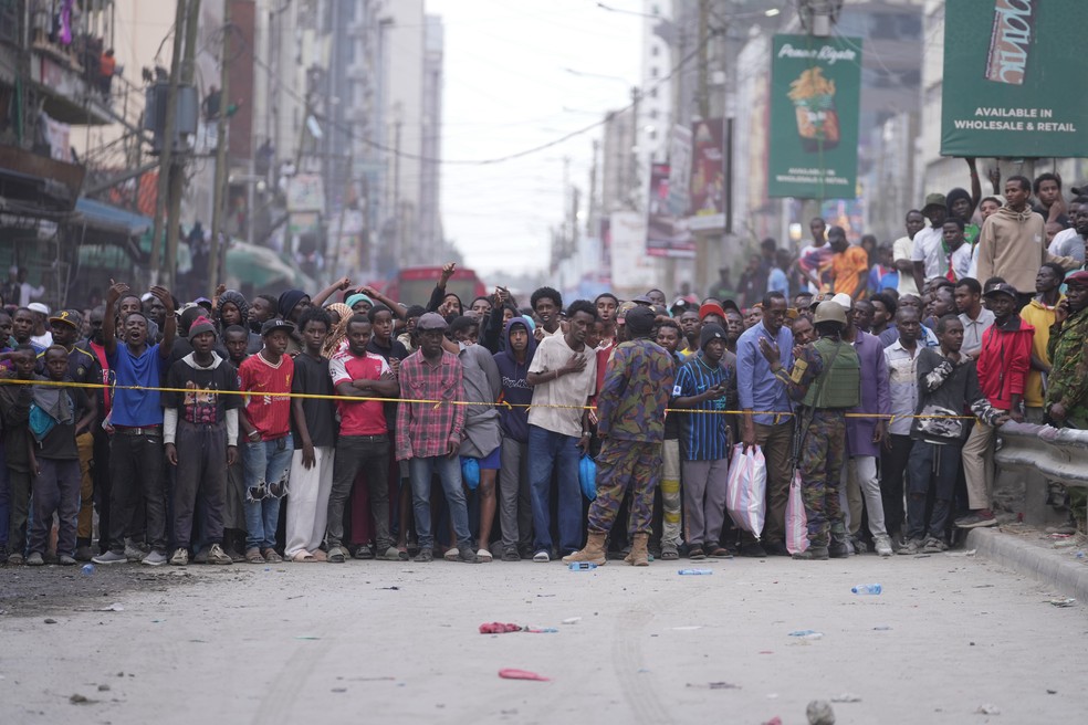 Pessoas observam por trás de um cordão de segurança após o desabamento de um prédio de vários andares em Nairóbi, Quênia — Foto: Brian Inganga/AP
