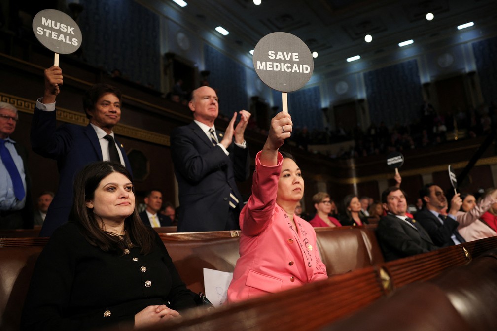 Deputados democratas seguram placas com dizeres "Salvem o Medicaid" e "Musk rouba" durante discurso de Donald Trump — Foto: Win McNamee/Pool via REUTERS.