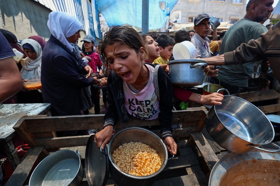 Menina recebe refeição enquanto outros esperam em ponto de distribuição em Nuseirat, no centro da Faixa de Gaza, em 2 de junho de 2025. — Foto: Eyad Baba/AFP