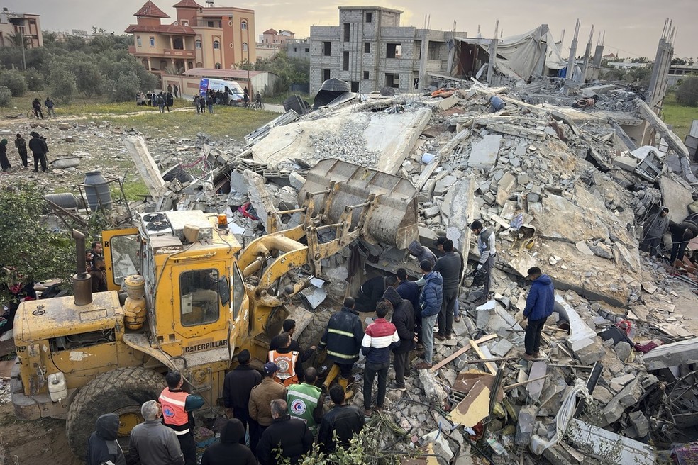 Voluntários e equipes de resgate usam uma escavadeira para remover os escombros de prédio destruído em Gaza — Foto: AP Photo/Mariam Dagga