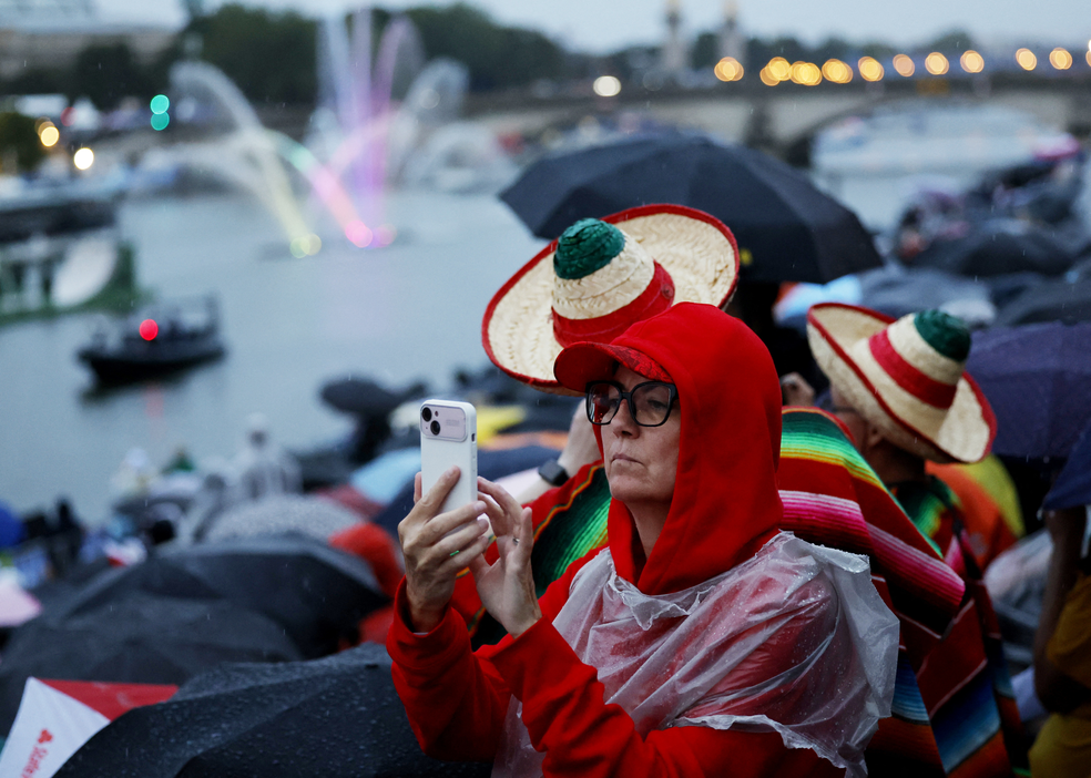 Mulher tira foto de abertura dos Jogos Olímpicos em Paris em 26 de julho de 2024. — Foto: Stefan Wermuth/Pool Photo via AP