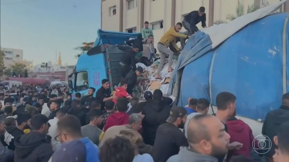 Palestinos desalojados correm para buscar água de um caminhão de ajuda — Foto: JN