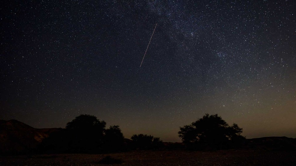Meteoro corta o céu com a Via Láctea vista à direita nas primeiras horas da manhã,  — Foto: Menahem Kahana / AFP Photo