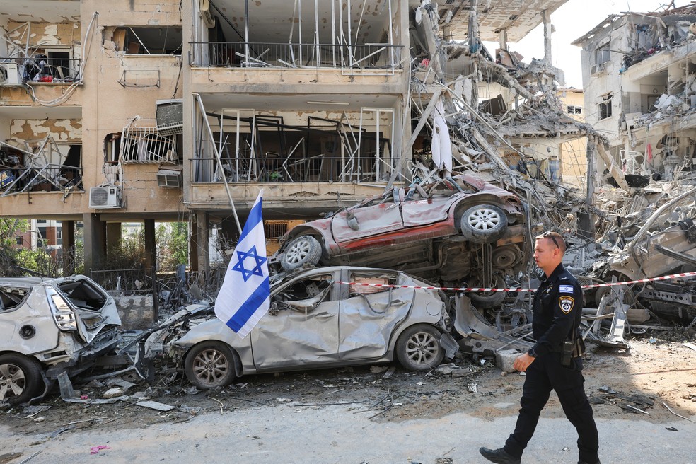 Policial caminha em frente a prédio e veículos destruídos por ataque do Irã à cidade de Ramat Gan, em Israel — Foto: REUTERS/Ronen Zvulun