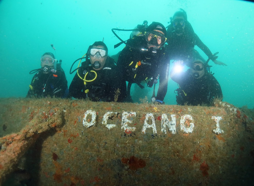 Mergulhadores fazem foto mostrando a carcaça que indica o nome do Oceano I. — Foto: Acqua Sub