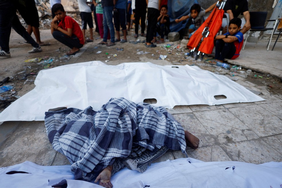 Crianças observam corpo de menina retirada dos escombros de prédio que desabou em Gaza — Foto: REUTERS/Mahmoud Issa