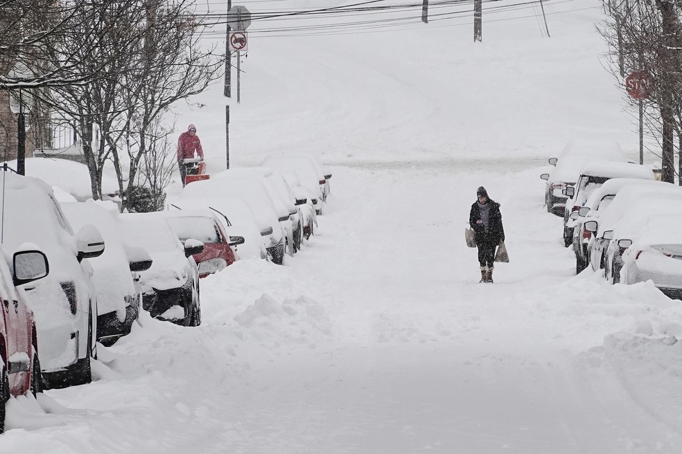 Uma pessoa carrega sacolas de compras por uma rua residencial durante uma tempestade de inverno, no domingo, em Cincinnati, nos EUA — Foto: AP Photo/Joshua A. Bickel