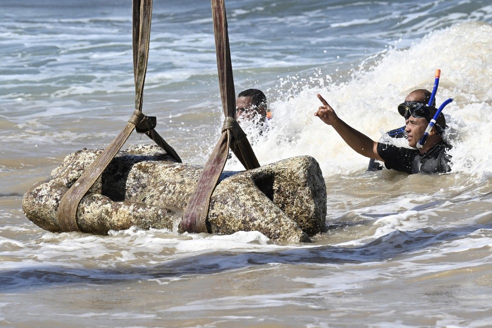 Mergulhadores observam enquanto um guindaste puxa uma estátua das águas da baía de Abu Qir, em Alexandria, no dia 21 de agosto de 2025, como parte de um evento organizado pelo Ministério do Turismo e das Antiguidades para recuperar antiguidades submersas — Foto: Khaled DESOUKI / AFP