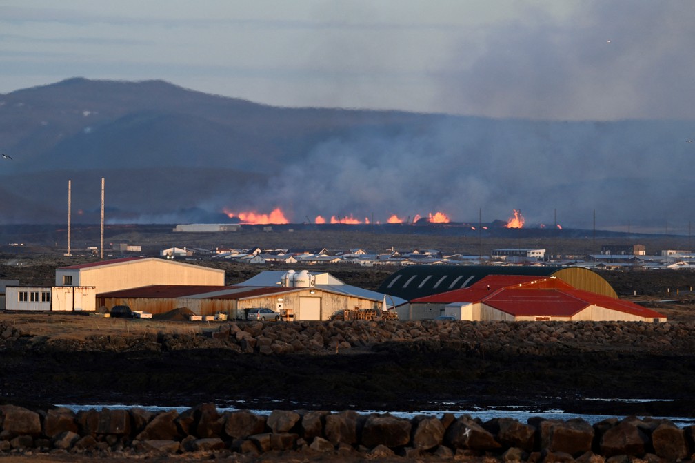 Um complexo industrial é visto em primeiro plano enquanto a lava de uma vulcão é expelida perto da cidade de Grindavik, no sudoeste da Islândia, após uma erupção neste domingo, 14 de janeiro de 2024. — Foto: Halldor KOLBEINS/AFP