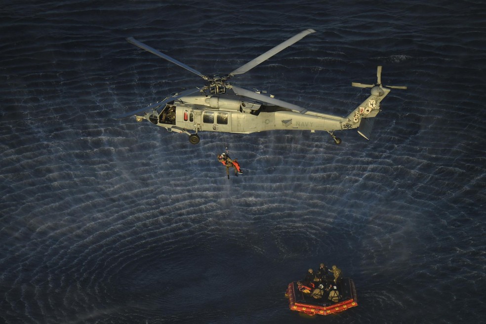 Mergulhadores da Marinha dos EUA e os astronautas da Artemis II, a bordo de um bote inflável, são alcançados por helicópteros e içados até o navio de resgate após deixarem a nave Orion, da NASA — Foto: NASA/James Blair