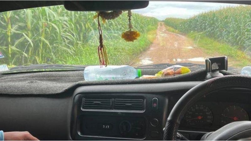 A vista do para-brisa de um carro mostra uma trilha de terra passando por plantaes de milho — Foto: NOPPORN WICHACHAT