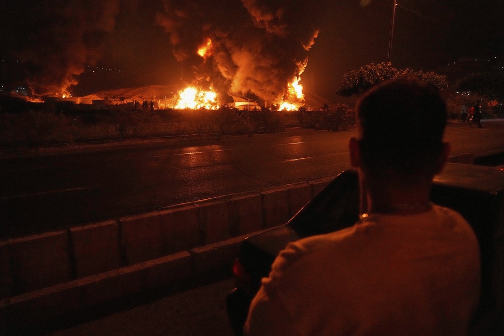 Um homem observa as chamas subindo de uma instalação de armazenamento de petróleo após ataque israelense em Teerã, Irã, na madrugada de domingo, 15 de junho de 2025 — Foto: AP Photo/Vahid Salemi