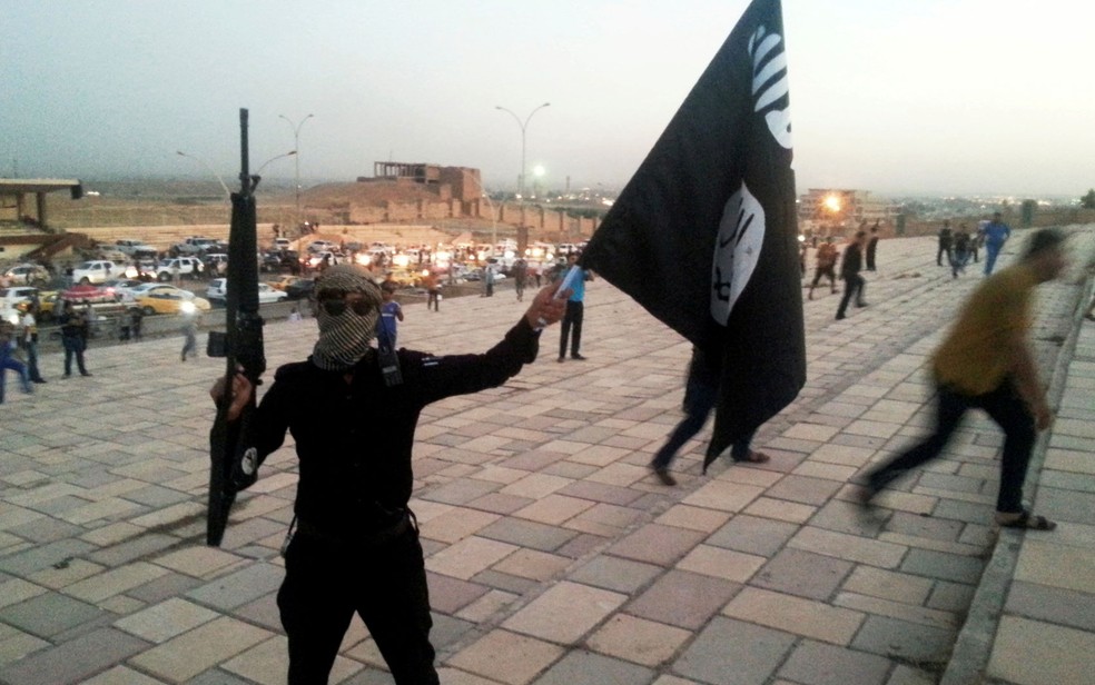 Combatente do Estado Islâmico exibe arma e bandeira do grupo em rua de Mossul, no Iraque, em foto de 23 de junho de 2014 — Foto: Reuters/Stringer